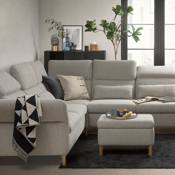 Modernes graues Sektionssofa mit verstellbaren Kissen, schwarz/weißer Decke, Fensternah, dunkler Teppich, Ottomane mit Snacks.
