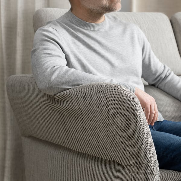 Mann sitzt auf grauem FAMMARP-Sofa, Arm auf Auflage, trägt grauen Pullover und Jeans.