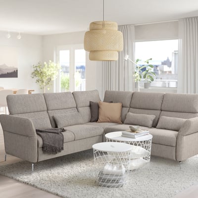 Ein modernes Wohnzimmer mit FAMMARP-Sektionssofa, Couchtischen, Pendelleuchte, Teppich und Topfpflanzen. Große Fenster zeigen ein Stadtbild.