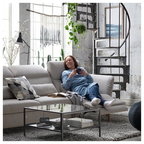 Eine Frau auf einem beigen FAMMARP-Sofa, mit einem Tablet, mit einer Wendeltreppe und einem großen Fenster in einem modernen Raum im Industriestil.