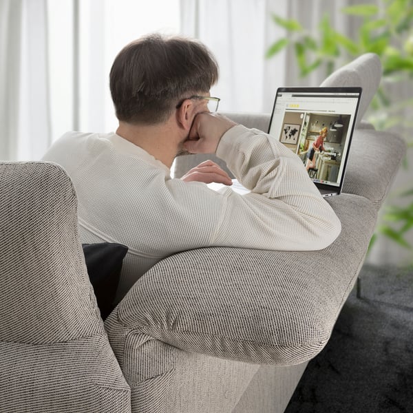 Mann sitzt auf einem grauen FAMMARP-Sofa und schaut auf einen Laptop mit verstellbaren Kopfstützen.