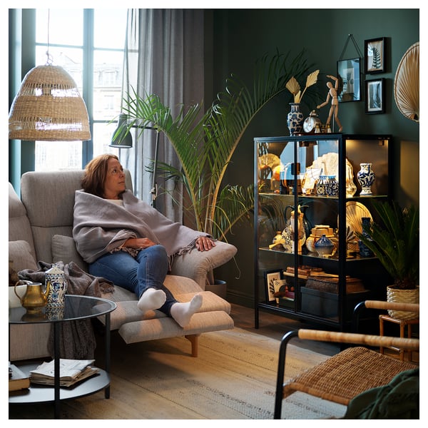 Ältere Frau, die sich im FAMMARP-Sofa in einem gemütlichen Zimmer mit Pflanzen und Dekor entspannt.