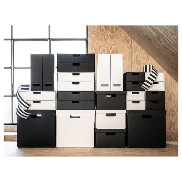 Gestapelte schwarz-weiße Aufbewahrungsboxen. Die Boxen variieren in der Größe und sind ordentlich auf Holzböden und Sperrholzwänden angeordnet. Modernes und minimalistisches Design.