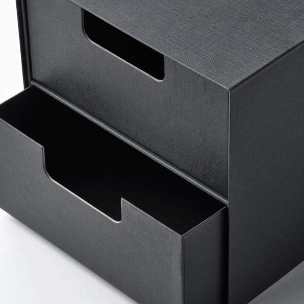 Schwarzer Mini-Aufbewahrungsschrank mit Schubladen aus strukturiertem Karton; glatte Griffe, abwechselnd offene und geschlossene Positionen, gepflegtes und modernes Design.