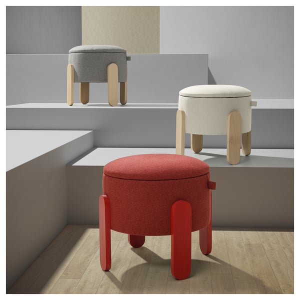 Drei runde Hocker in Rot, Beige und Grau mit Holzbeinen, die auf einem Gestell ausgestellt sind.