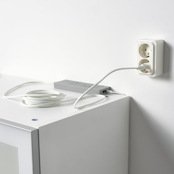 Weißes Netzteil, das in die Steckdose eingesteckt wird und LED-Streifen für die Beleuchtung mit Strom versorgt.