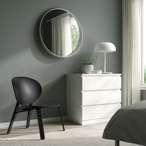 Minimalistisches Schlafzimmer mit Stuhl, Kommode, Spiegel, Pilzlampe, hellgrünen Wänden.