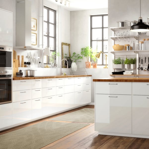 Moderne weiße Küche mit Holztheken, großen Fenstern, eleganten Geräten und Teppich.