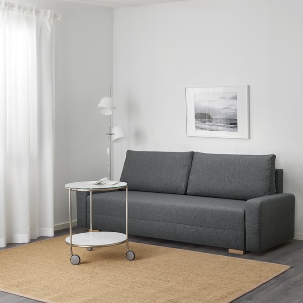 Ein modernes Wohnzimmer, ein graues GRÄLVIKEN-Schlafsofa mit Beistelltisch und Lampe. Das Schlafsofa lässt sich in ein Bett verwandeln und verfügt über Stauraum unter dem Sitz.