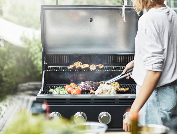 Frau grillt buntes Gemüse im Freien.