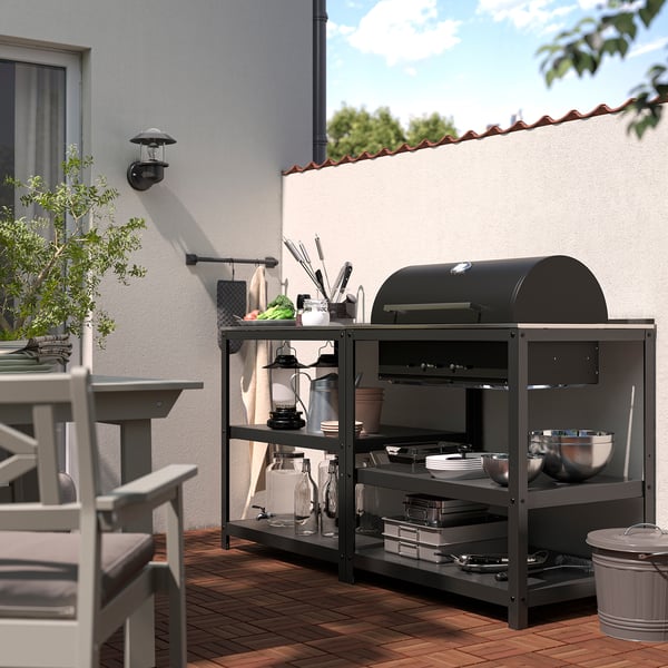 Schwarzer Holzkohlegrill mit Thermometer und isolierten Griffen sowie eine Kücheninsel aus Metall zum Kochen und Unterhalten im Freien.