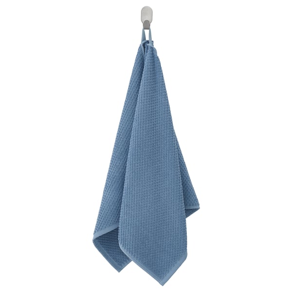 An einem Haken hängt ein blaues GULVIAL Handtuch. Hergestellt aus weicher, flauschiger Baumwolle, ist es gefaltet und hat eine strukturierte Oberfläche.