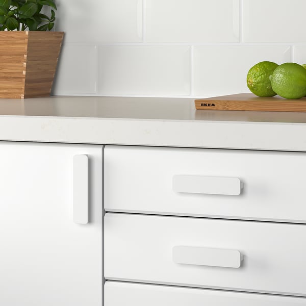 Moderne Küchenschränke mit weißen Griffen, glatt verarbeitet. Zwei grüne Früchte auf einem hölzernen Schneidebrett, die den cleanen, minimalistischen Stil ergänzen.