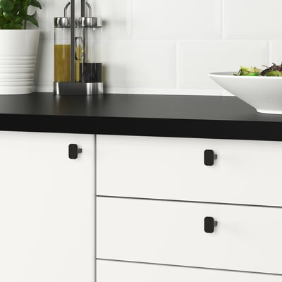 Moderne Küchenschränke mit schwarzen HACKÅS-Knöpfen, glatt anzufassen, auf weißen Schubladen mit schwarzer Arbeitsplatte.