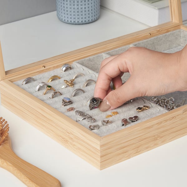 Eine Hand, die einen Ring aus einer Schmuckschatulle aus Holz mit Fächern auswählt, in denen verschiedene Ringe und kleine Accessoires ausgestellt sind.