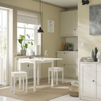 Moderne Küche mit weißer HOUGA-Essgarnitur, einschließlich Tisch und Hockern. Weiche beige Wände, große Fenster und minimalistisches Dekor.