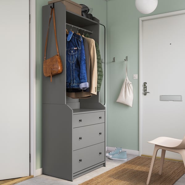 Moderner grauer HOUGA-Kleiderschrank mit Schubladen, Kleiderbügeln und Haken, mit Jeansjacke, Tasche und Turnschuhen, vor Salbeiwänden.