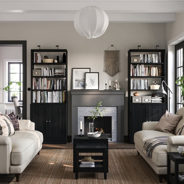Modernes Wohnzimmer mit schwarzem HAVSTA-Bücherregal, cremefarbenen Sofas, grauem Teppich und Kamin.