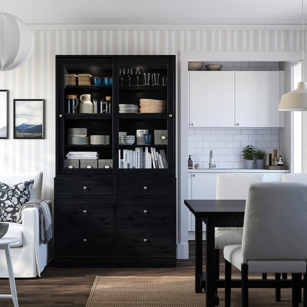 Modernes Wohnzimmer mit schwarzem HAVSTA-Schrank, Glastüren, weißer Küche, Couch, Stühlen, Esstisch.
