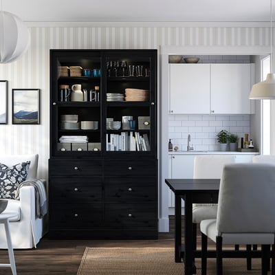 Modernes Wohnzimmer mit schwarzem HAVSTA-Schrank, Glastüren, weißer Küche, Couch, Stühlen, Esstisch.