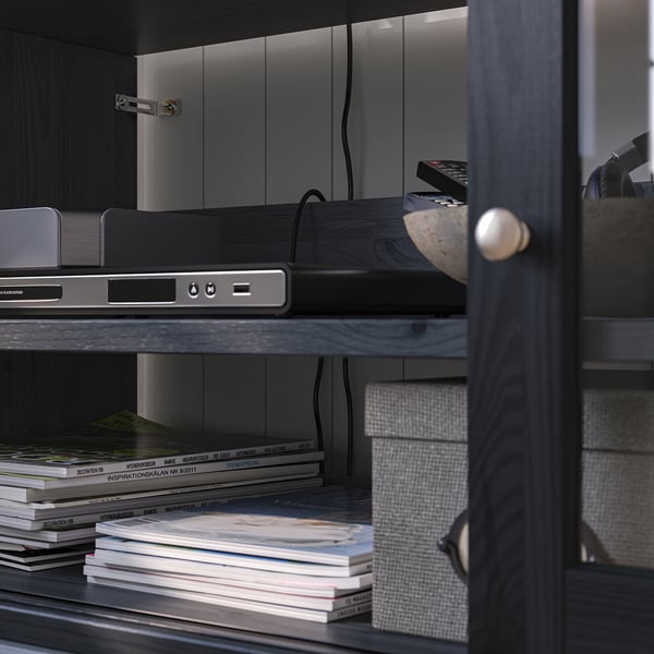 Schwarzer TV-Schrank aus Holz mit Regalen, in denen Elektronik und gestapelte Zeitschriften untergebracht sind, dunkles Interieur.