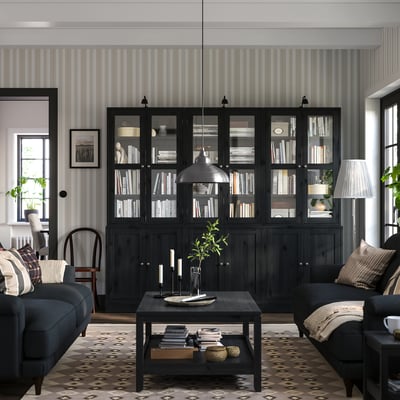 Modernes Wohnzimmer mit schwarzen HAVSTA-Bücherregalen, eleganten Möbeln und gemustertem Teppich.