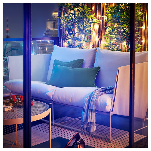 Ein moderner Balkon mit HAVSTEN-Sofa, Kissen, Überwurf und Blumen.