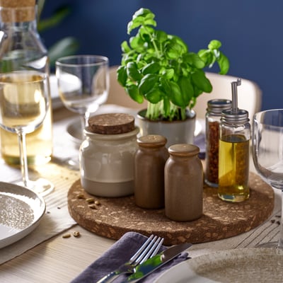 Ein dunkelbrauner Korkuntersetzer hält Gläser, Kräuter und Gläser auf dem Esstisch.