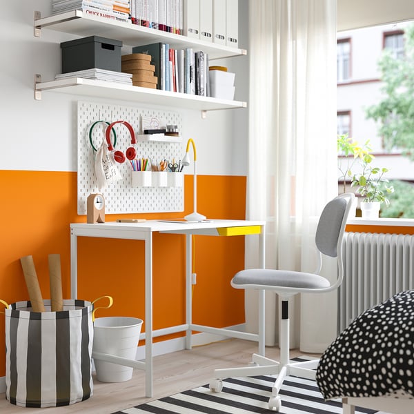 Weißer Metallschreibtisch mit Schubladen im modernen Büro, nahe dem Fenster mit orangefarbener Akzentwand.