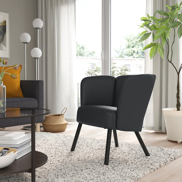 Modernes Wohnzimmer mit schwarzem HERRÅKRA-Stuhl, grauer Couch, gesprenkeltem Teppich, Couchtisch und hoher Pflanze am Fenster.