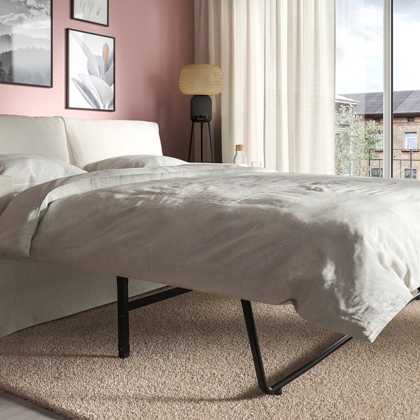 Modernes Schlafsofa im Wohnbereich. Graue Polsterung, schwarze Metallbeine. Verwandelt sich von Sitzgelegenheiten in Schlafmöglichkeiten. Großes Fenster mit Vorhängen daneben.