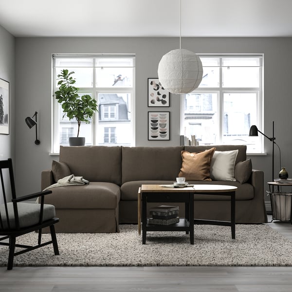 Modernes Wohnzimmer mit HYLTARP-Sofa in Braun, großem Fenster, weißer Lampe, Pflanze und Accessoires.