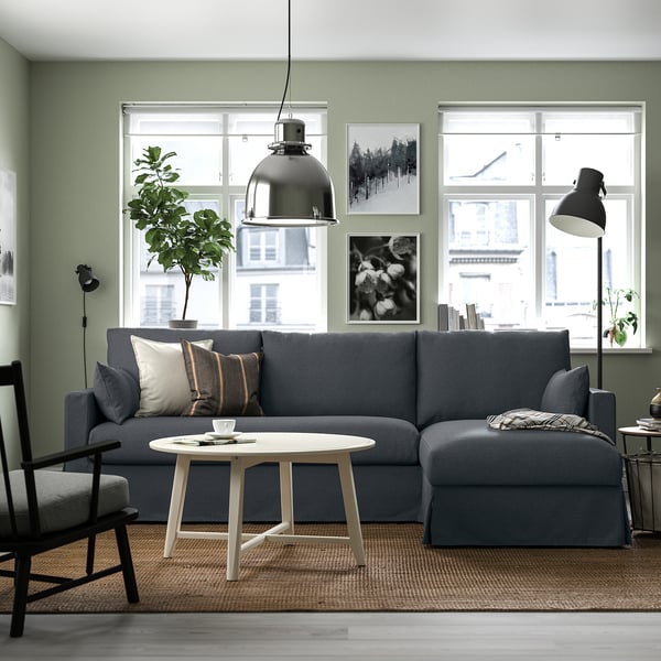 Modernes Wohnzimmer mit großem grauem Sofa, Aufbewahrungschaiselongue, weißem Couchtisch, schwarzer Stehlampe, grüner Wand, Kunst, Fenster und Pflanze.