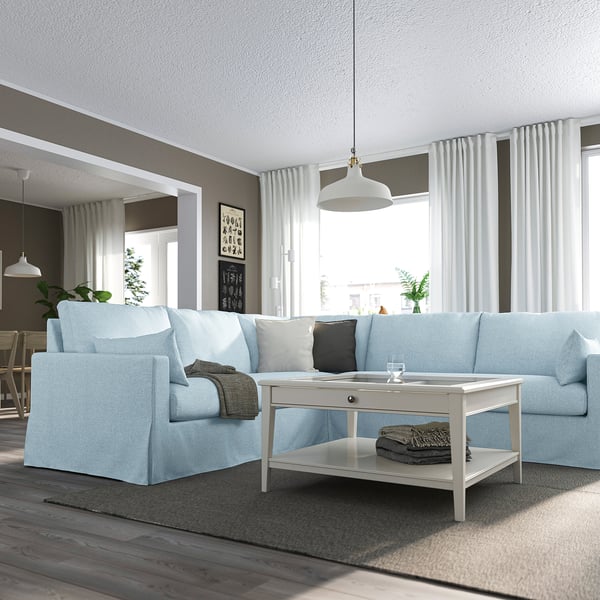 Großes hellblaues Sektionssofa mit weißem Couchtisch, gewölbter Lampe, grauen Decken und weißen Vorhängen in modernem Wohnbereich.