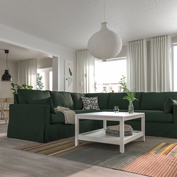 Modernes Wohnzimmer mit grünem Sofa, Couchtisch, Teppich und großem Fenster. Pflanzen und Kissen sorgen für Gemütlichkeit.