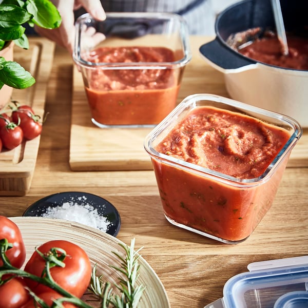 Tomatensaucenbehälter auf Holzbrettern mit frischen Tomaten und Kräutern.