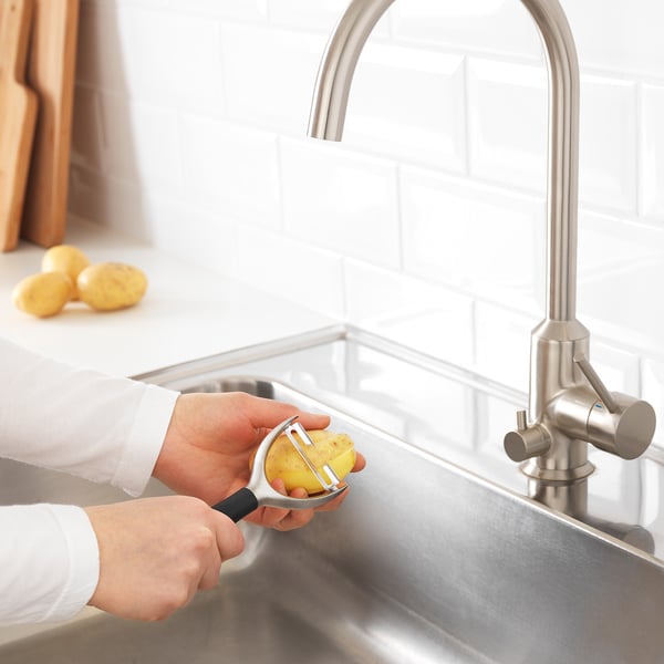Kartoffel mit IKEA Sparschäler von Hand über das Waschbecken schälen. Edelstahlarmatur und Arbeitsplatte sichtbar.