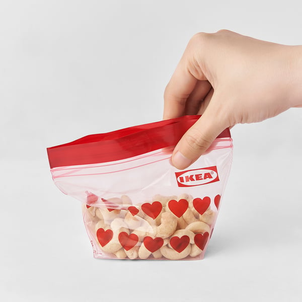 Die Hand hält eine rot versiegelte IKEA-Tasche, mit Herzen und Snacks darin.