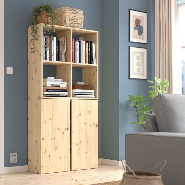 IVAR Bücherregal aus hellem Holz an blauer Wand, gefüllt mit Büchern. Neben einem grauen Stuhl, einer kleinen Pflanze und gerahmten Bildern.
