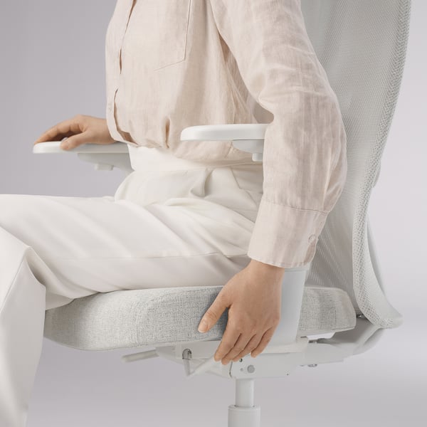 Person, die auf einem weißen, ergonomischen Bürostuhl sitzt und die Sitzhöhe einstellt.