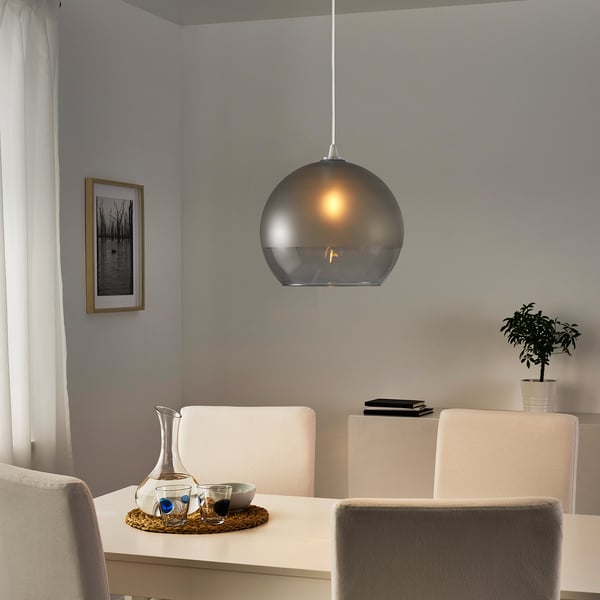 Moderner Essbereich mit Glas-Pendelleuchte über weißem Tisch und beigen Stühlen, Tablett mit Krug und Gläsern.