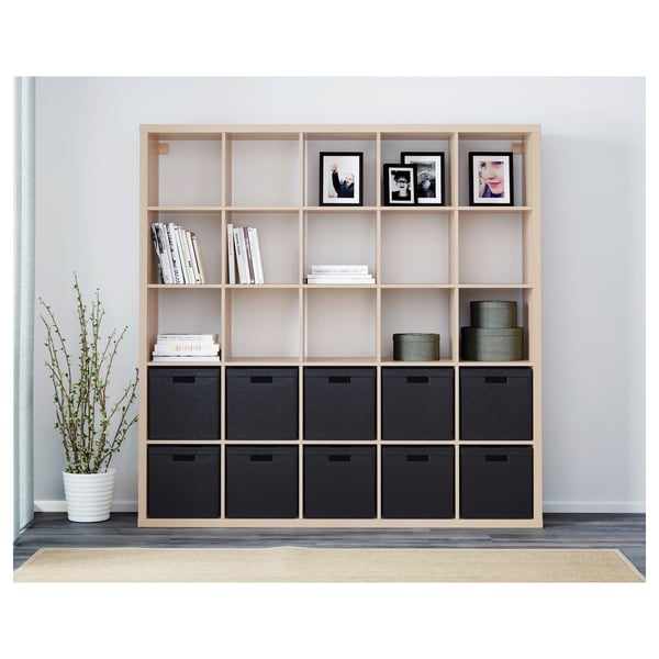 Ein KALLAX Regal aus Holz mit schwarzen Aufbewahrungsboxen und offenen Regalen, in denen Bücher und gerahmte Fotos ausgestellt sind.