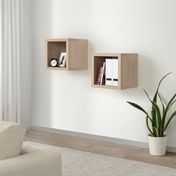KALLAX Wandregale, helles Holz. Kleine, quadratische Würfel nehmen Bücher und Uhr auf. Daneben ein beiger Stuhl und eine Pflanze.