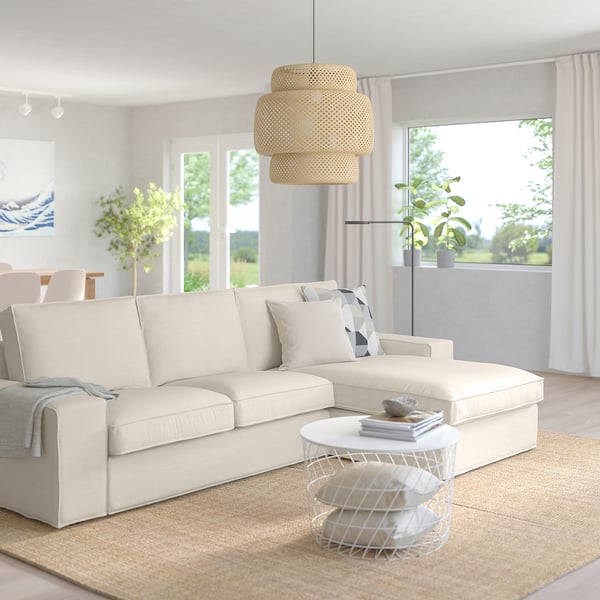 Modernes Wohnzimmer mit cremefarbenem KIVIK-Sofa, weißem Couchtisch, neutralem Dekor, großen Fenstern und beigem Teppich.