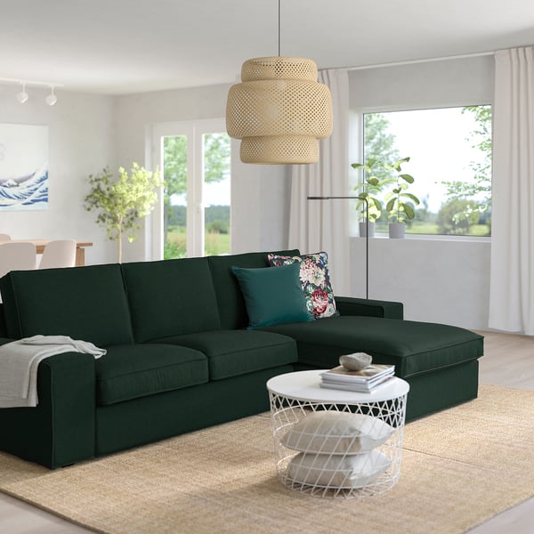 Modernes Wohnzimmer mit großem dunkelgrünem KIVIK-Sofa, Blumenkissen, weißem Beistelltisch, großem Fenster und einzigartiger Pendelleuchte.