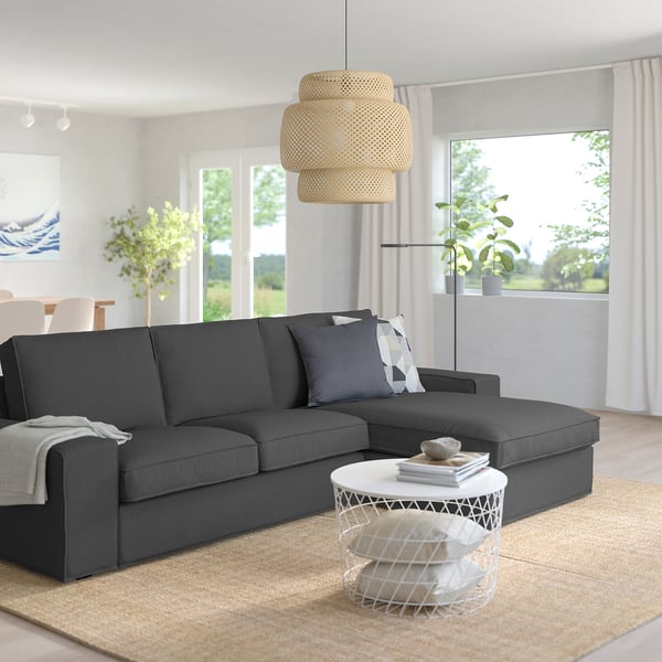 Modernes Wohnzimmer mit grauem KIVIK-Sofa und weißem Couchtisch, großem Fenster, Pflanzen und geschichteter Pendelleuchte.