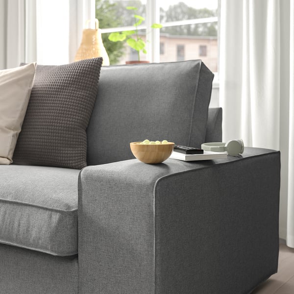 Graues Sofa mit Kissen, Schüssel, Fernbedienung und Kopfhörern an der Armlehne; Großes Fenster mit Vorhängen.