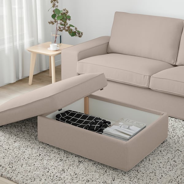 Beige KIVIK Fußhocker mit Stauraum, Zeitschriften, Decke, neben Sofa und Beistelltisch mit Vase und Teetasse. Helles, luftiges Fenster.