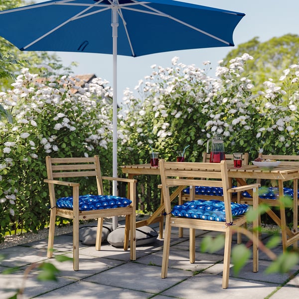 Sitzbereich im Freien mit blauen und weißen Tupfenkissen auf Holzstühlen, blauem Sonnenschirm, umgeben von weißen Blumen.
