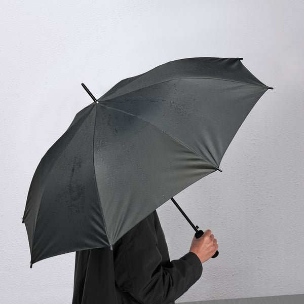 Person mit einem schwarzen KNALLA Regenschirm, der sich mit einer Hand automatisch öffnet.